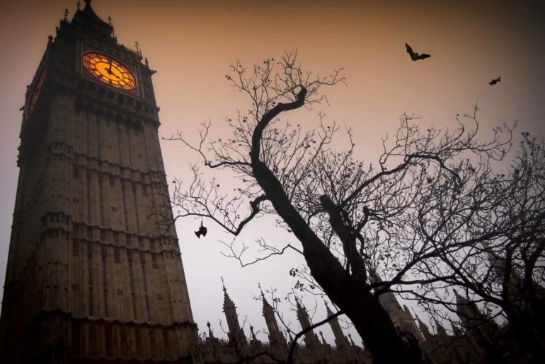 The spooky clock tower of Westminster with a bare tree and flying bats