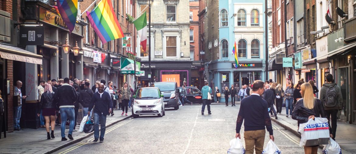 Shoppers walking down a Soho street in London's westend past a bar with a LGBT rainbow flag