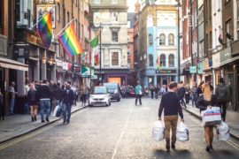 Shoppers walking down a Soho street in London's westend past a bar with a LGBT rainbow flag