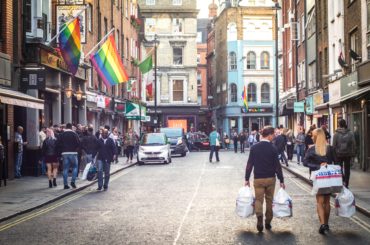 Shoppers walking down a Soho street in London's westend past a bar with a LGBT rainbow flag